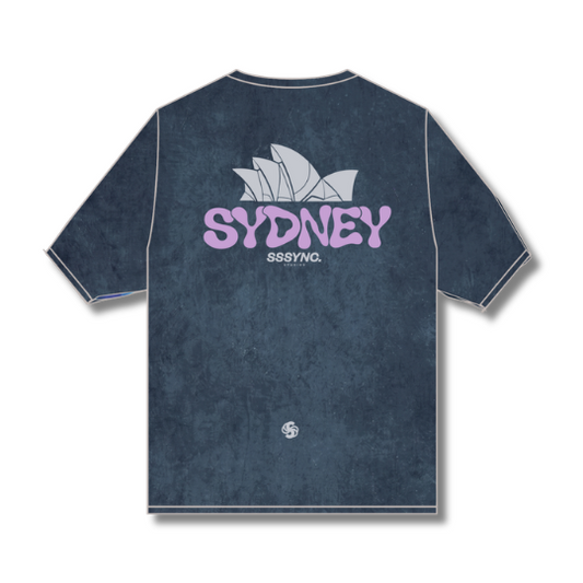 A dark blue textured t-shirt with a distressed finish, featuring a graphic on the back with a white Sydney Opera House silhouette, the word 'SYDNEY' in light purple, and 'SSB7NC.' underneath.