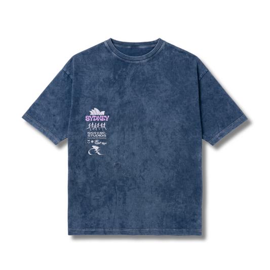 A blue acid-wash t-shirt with a distressed texture, featuring a white and purple graphic print on the left chest that reads 'SYDNEY 2026' and includes silhouettes of people and a kangaroo.